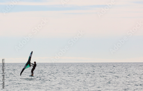 Man practicing wing foil with hydrofoil at sunset in the sea.