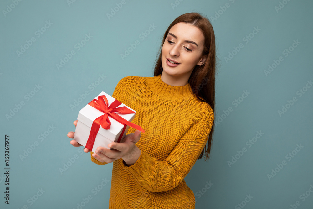 Shot of attractive positive smiling young brunette woman isolated over colourful background wall wearing everyday trendy outfit holding gift box and looking to the side Shot of attractive positive smiling young brunette woman isolated over colourful background wall wearing everyday trendy outfit holding gift box and looking to the side