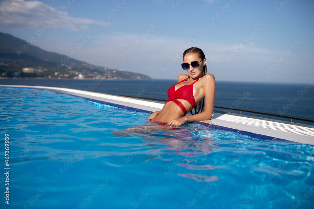 Young woman relaxing in infinity swimming pool looking at view. Summer time, beach, pool, vacation concept