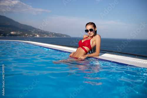 Young woman relaxing in infinity swimming pool looking at view. Summer time, beach, pool, vacation concept