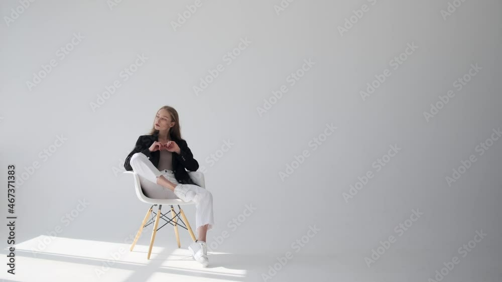 Beautiful woman in blazer sitting on chair and looking away over white background