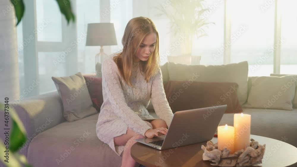 Young caucasian woman typing on laptop and using smartphone while sitting on comfy couch. Happy female blonde with modern gadgets at home. Young caucasian woman typing on laptop and using smartphone while sitting on comfy couch. Happy female blonde with modern gadgets at home.