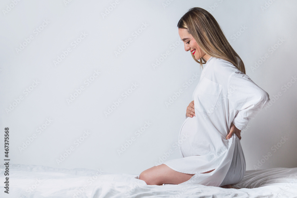 Positive pregnant woman with hand on back sitting on bed Positive pregnant woman with hand on back sitting on bed
