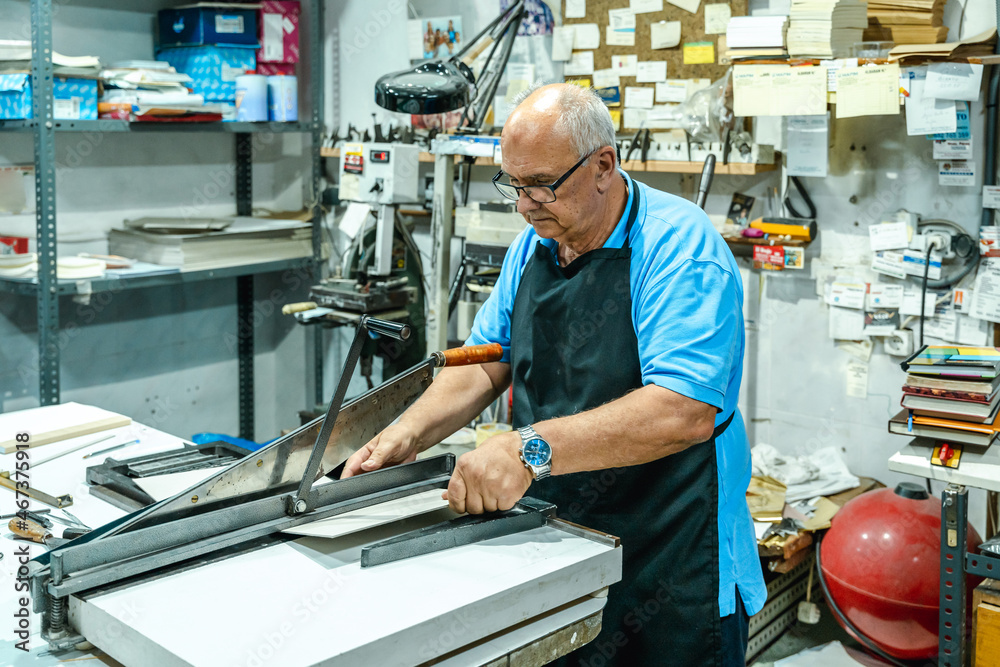 Serious senior male master operating on cutting machine in workshop Serious senior male master operating on cutting machine in workshop