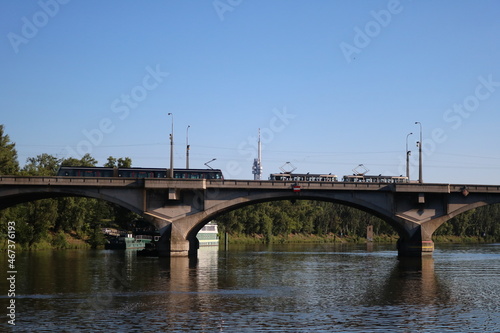 Trams on the bridge over the Vltava River against the background of the Zhizhkov TV  tower (Žižkovský vysílač) and green trees and blue summer sky