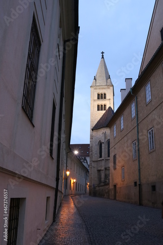 An old church on a narrow cobblestone street in Prague's Hradcany lit by gas lanterns in the early morning