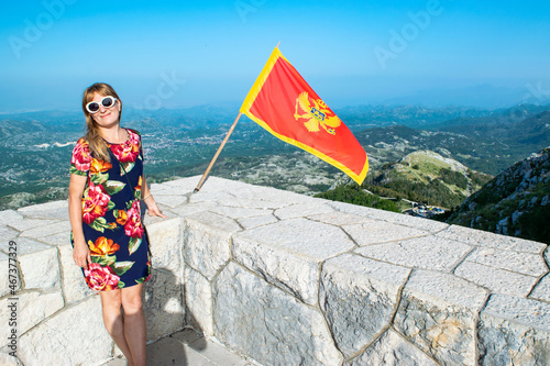 Tourist woman and waving flag of Montenegro against background  mountains near Njegos mausoleum. Lovcen National Park. Montenegro. photo