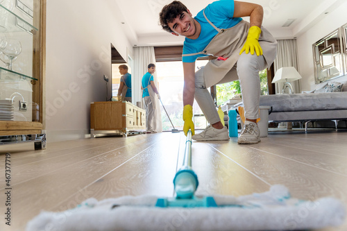 Happy male professional housekeeper washing floor with mop in living room photo