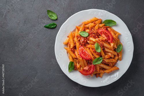 Penne pasta with bolognese sauce and basil in a white plate on a brown background.