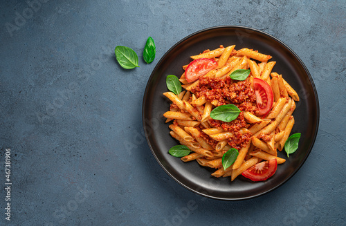 Pasta with bolognese sauce, fresh basil and tomatoes in a black plate on a graphite background.