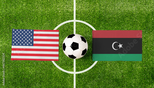 Top view soccer ball with USA vs. Libya flags match on green football field.