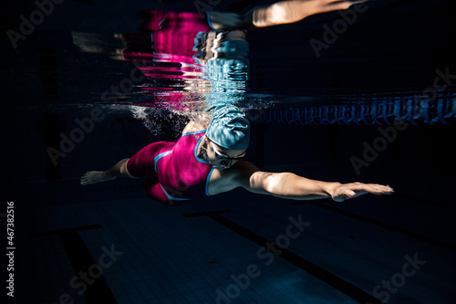 Fototapeta Naklejka Na Ścianę i Meble -  One female swimmer in swimming cap and goggles training at pool, indoors. Underwater view of swimming movements details.