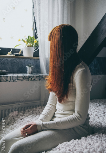 Eine Frau sitzt alleine auf ihrem Bett und schaut aus dem Fenster.