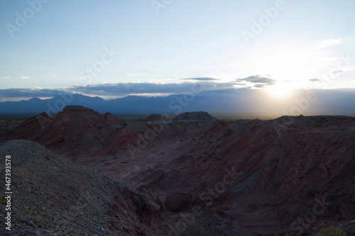 The red canyon and valley at sunset. Panorama view of the arid desert  sandstone formations  rocky mountains  lens flare and hiding sun in Talampaya national park in La Rioja  Argentina.