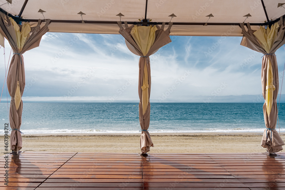 Vista desde el interior de una pérgola con suelo de madera y dos ventanales  con continas