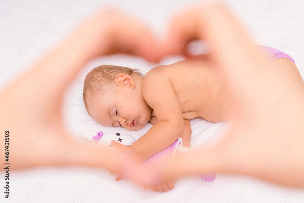 A sleeping baby with his favorite knitted toy. Selective focus on the child through the hands of the mother making a heart-shaped gesture with her hands A sleeping baby with his favorite knitted toy. Selective focus on the child through the hands of the mother making a heart-shaped gesture with her hands