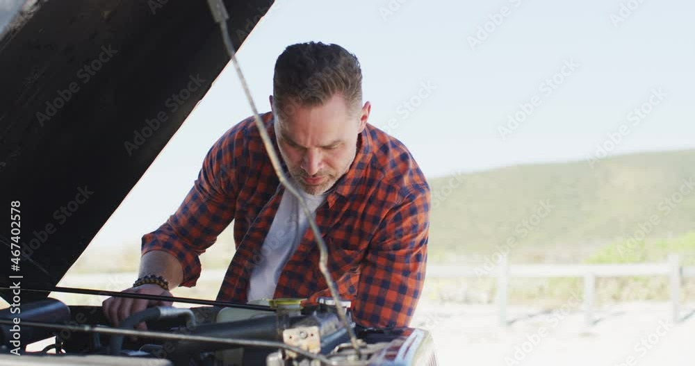 Stressed caucasian man looking at broken down car with open bonnet on sunny day at the beach Stressed caucasian man looking at broken down car with open bonnet on sunny day at the beach