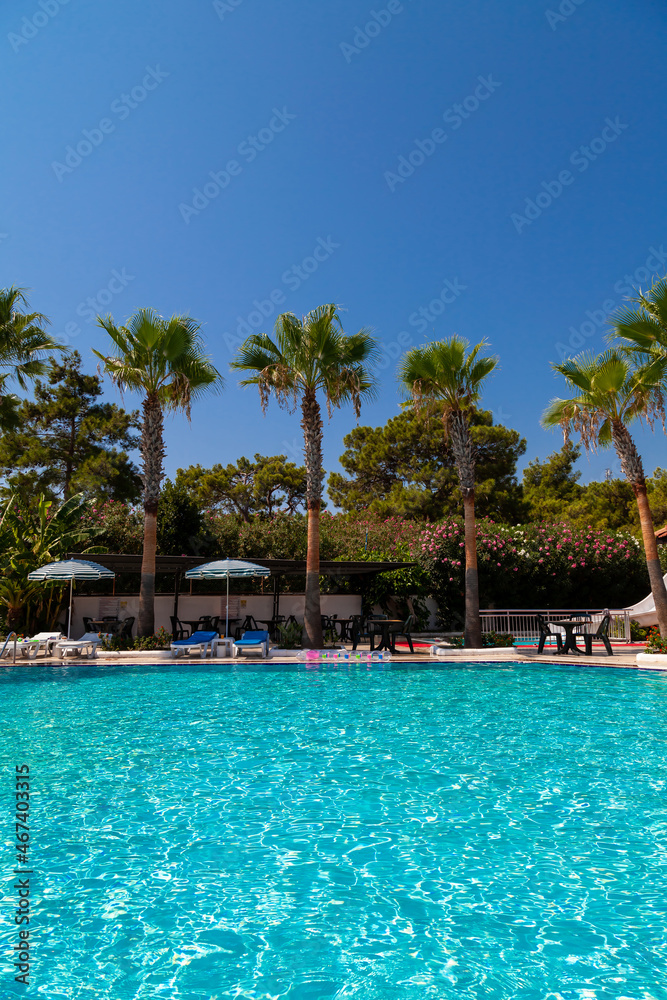 Hotel with swimming pool, palm trees and pines. Tourists rest on sunbeds under umbrellas. Travel in the pandemic Hotel with swimming pool, palm trees and pines. Tourists rest on sunbeds under umbrellas. Travel in the pandemic