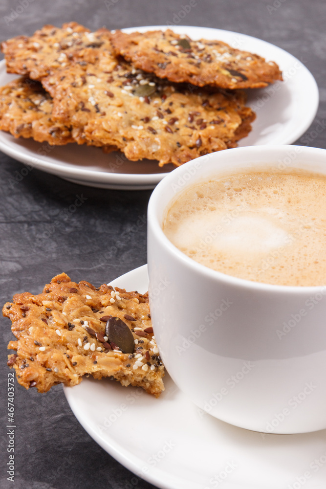 Cup of coffee with milk and fresh baked oatmeal cookies on white plate. Delicious crunchy dessert Cup of coffee with milk and fresh baked oatmeal cookies on white plate. Delicious crunchy dessert