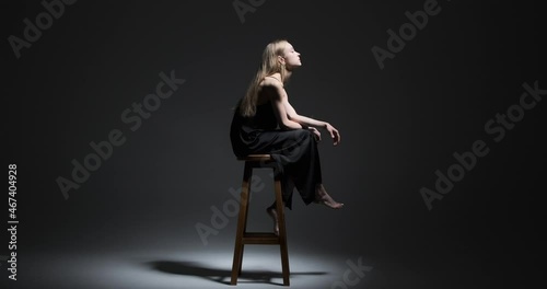 Profile of beautiful fashion model sitting on stool over black background photo