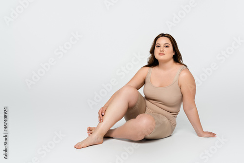 Young body positive woman looking at camera while sitting on grey background.