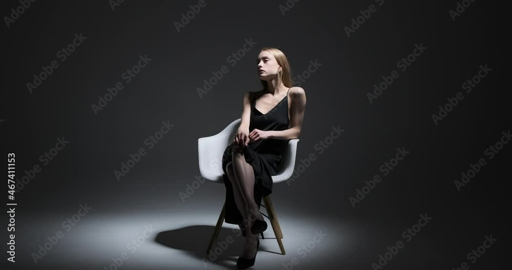 Beautiful fashion model sitting on chair with legs crossed over black background Beautiful fashion model sitting on chair with legs crossed over black background