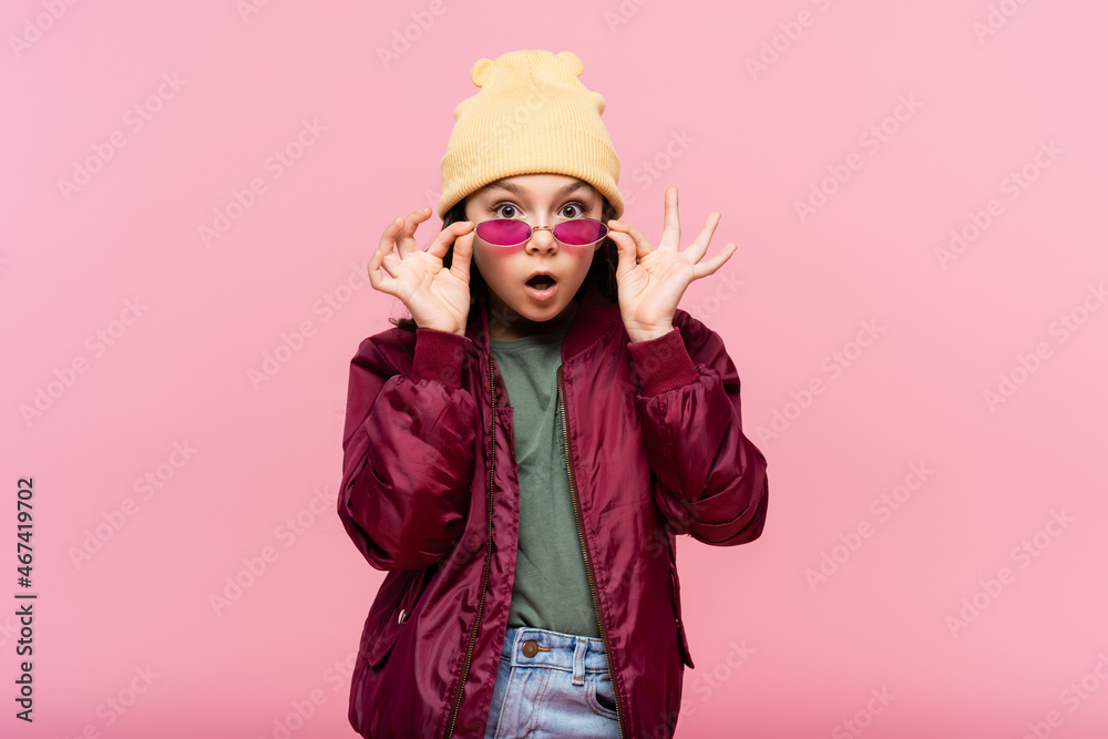 surprised preteen girl in trendy outfit adjusting sunglasses isolated on pink. surprised preteen girl in trendy outfit adjusting sunglasses isolated on pink.