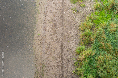 Top down view on a river and a river bank. Wet dirt, small stones and green grass is visible. The water is clear and stones underwater create a natural background. Abstract transition in the nature.
