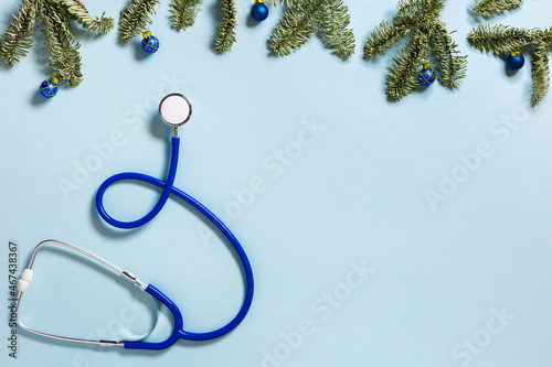 Blue stethoscope with green fir tree branches. Winter holidays medical background blue colored with copy space. View from above.