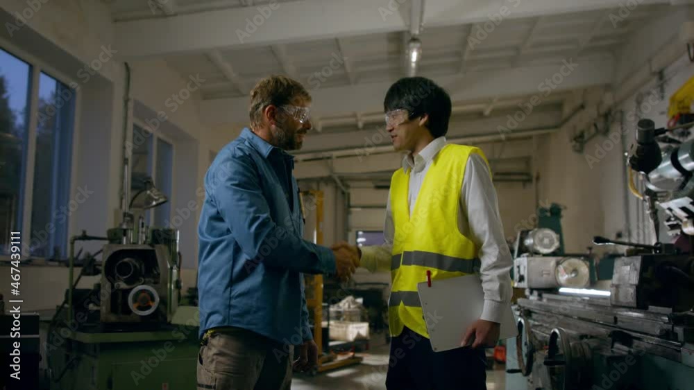 Japanese engineer shaking hands with mature wroker indoors in metal workshop. Japanese engineer shaking hands with mature wroker indoors in metal workshop.
