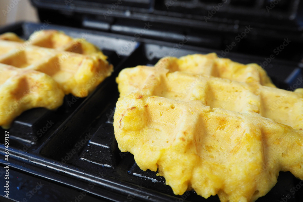 two ready-made Belgian waffles made from corn flour, eggs and pumpkin, lying in a waffle iron during cooking. homemade gluten - free , lactose - free food . side view two ready-made Belgian waffles made from corn flour, eggs and pumpkin, lying in a waffle iron during cooking. homemade gluten - free , lactose - free food . side view