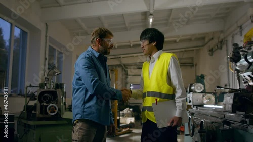 Japanese engineer shaking hands with mature wroker indoors in metal workshop. photo