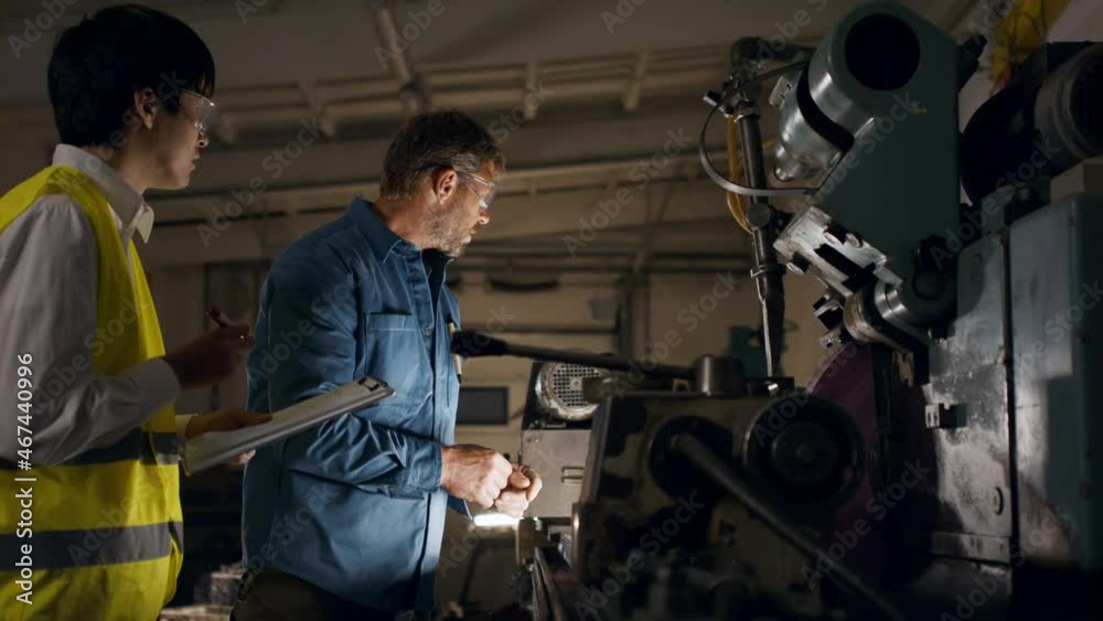 Japanese engineer controlling mature worker indoors in metal workshop. Japanese engineer controlling mature worker indoors in metal workshop.