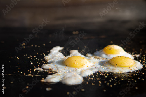 Three fried quail eggs on a hot flat top griddle. Pepper and oil steaming hot.