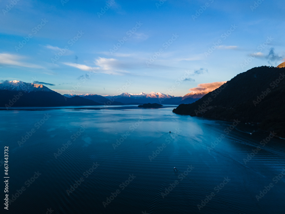 Aerial view of boats sailing and Lake Todos Santos with snow-capped mountains in the background at sunset.