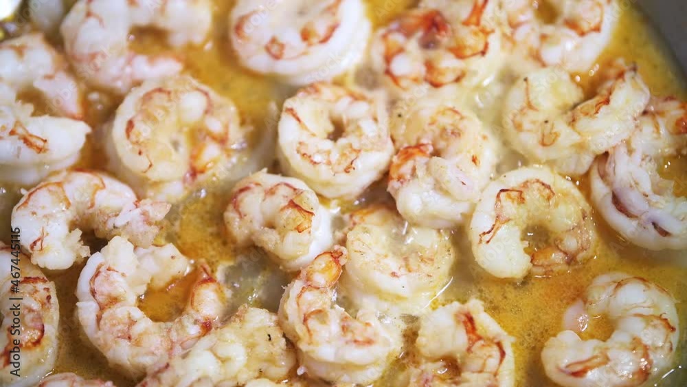 Macro closeup of stainless steel frying pan with sauteing olive oil, sweet onion slices and whole large king jumbo Argentinian shrimp seafood cooked on stove in sauce Macro closeup of stainless steel frying pan with sauteing olive oil, sweet onion slices and whole large king jumbo Argentinian shrimp seafood cooked on stove in sauce