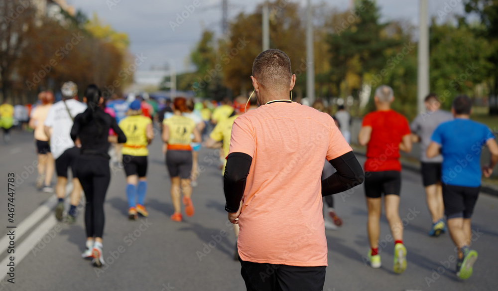 Obraz premium Man wearing sportswear and earphones running on city road with other people. Marathon race contestants. Concept of healthy lifestyle