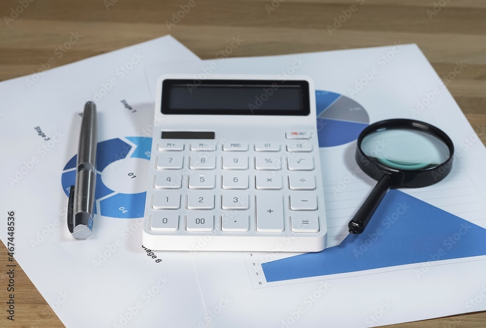 Calculator, magnifying lens on business paper documents withblue charts and graphs. Calculator, magnifying lens on business paper documents withblue charts and graphs.