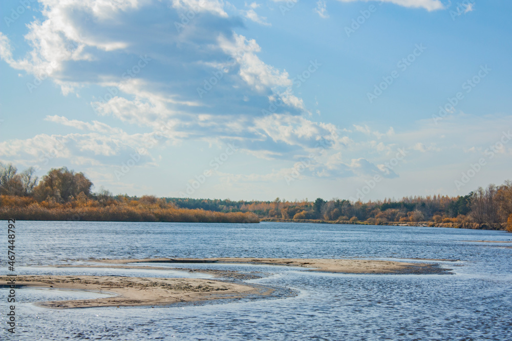 Beautiful clouds in the blue sky. Autumn landscape on a bright sunny day. Sandy islands on the river.