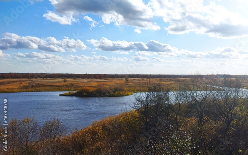 Beautiful autumn landscape in clear, sunny weather. Yellowed grass on the bank of a blue river under a bright, blue sky with clouds.