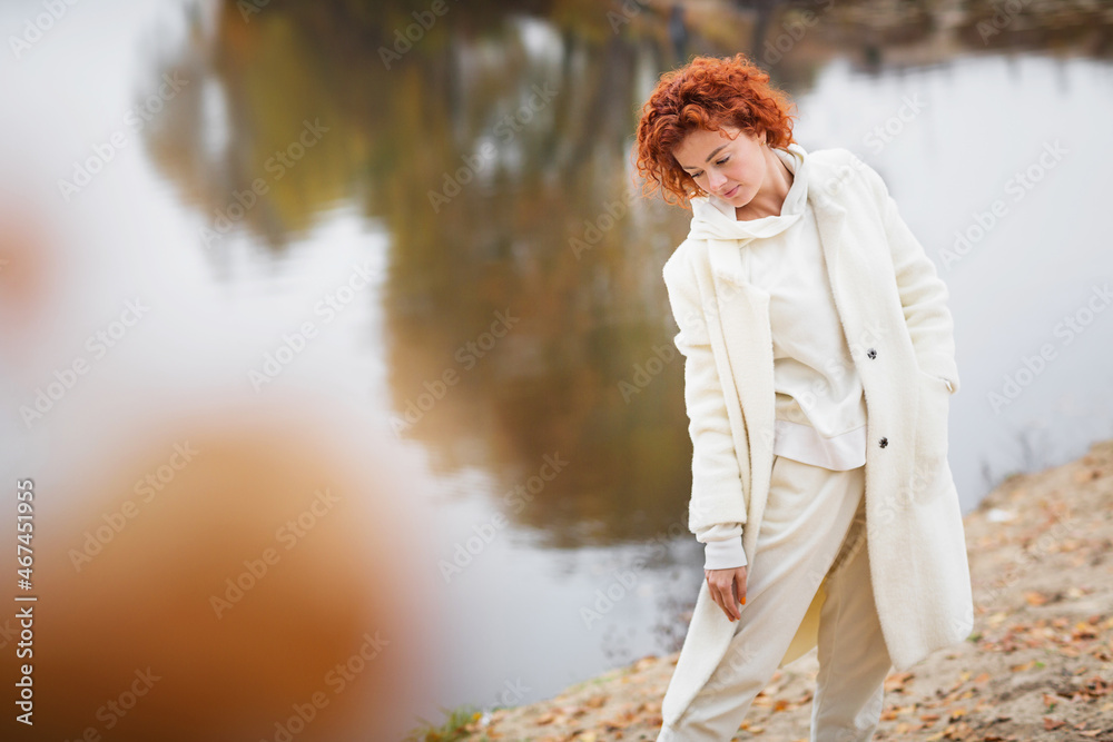 Beautiful redhead woman walking and relaxing outdoors in autumn around lake Beautiful redhead woman walking and relaxing outdoors in autumn around lake
