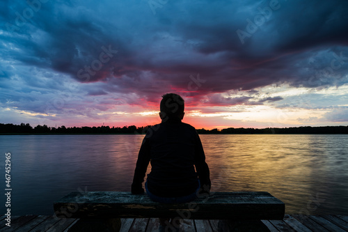 Fototapeta Naklejka Na Ścianę i Meble -  The boy stared at the setting sun by the lake.