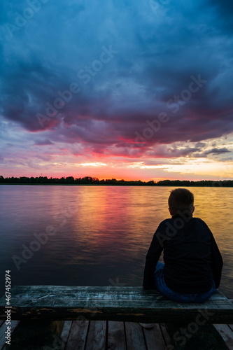 The boy stared at the setting sun by the lake.