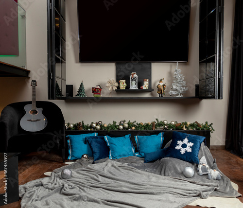 Christmas-themed cushions on a blanket on the floor of a living room, with a guitar by the side