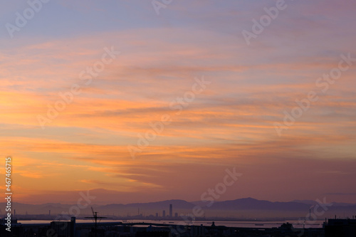 都市の夜明け。日の出とともに空と雲がオレンジ色に染まる。遠くに大阪湾を臨む