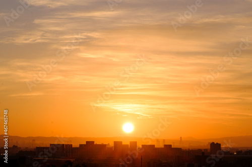 都市の夜明け。日の出とともに空と雲がオレンジ色に染まり、ビル群はシルエットとして写す