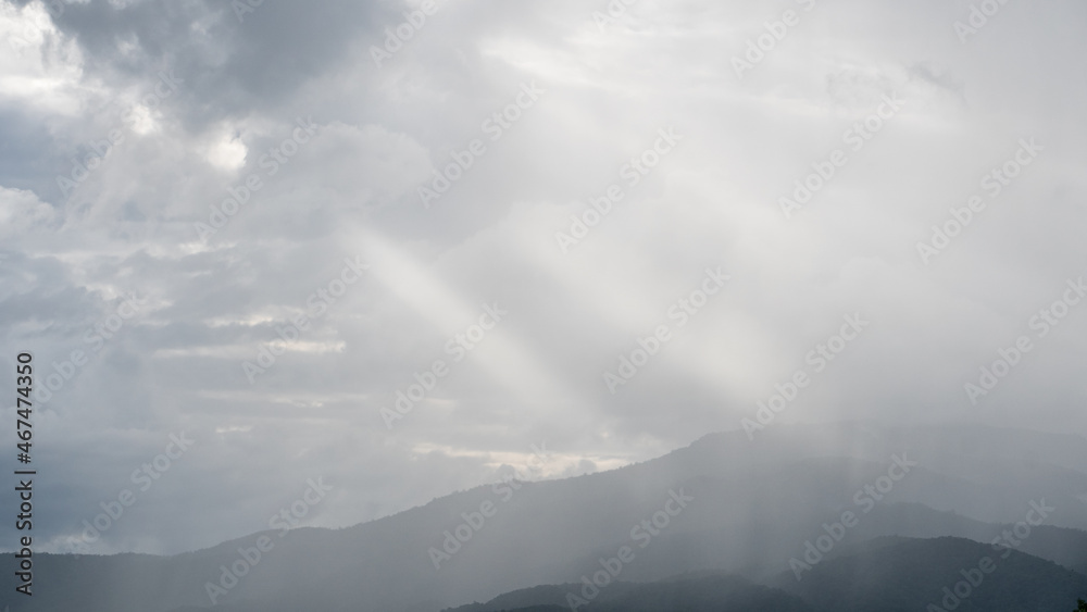 A view overlooking the mountains and the sky with clouds and light shining through.