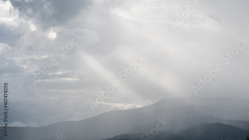 A view overlooking the mountains and the sky with clouds and light shining through.