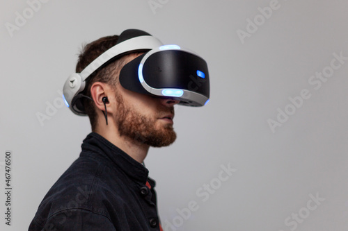 young man with beard in virtual reality helmet with gamepad joystick playing