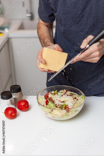 a young man with a beard 25-35 in a modern kitchen rubs cheese and prepares a salad
